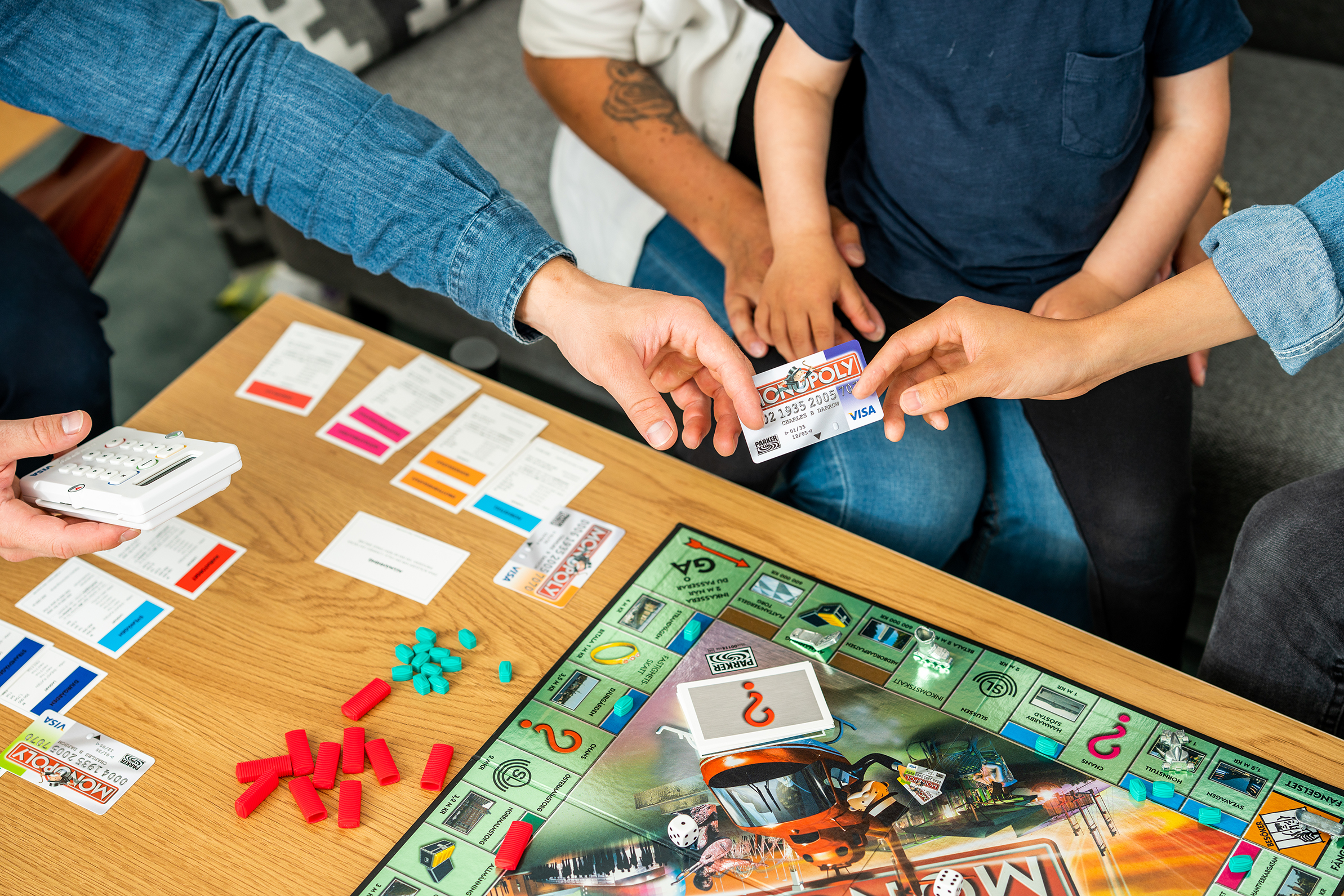 Barn och vuxna är mitt uppe i spelet Monopol runt soffbordet.