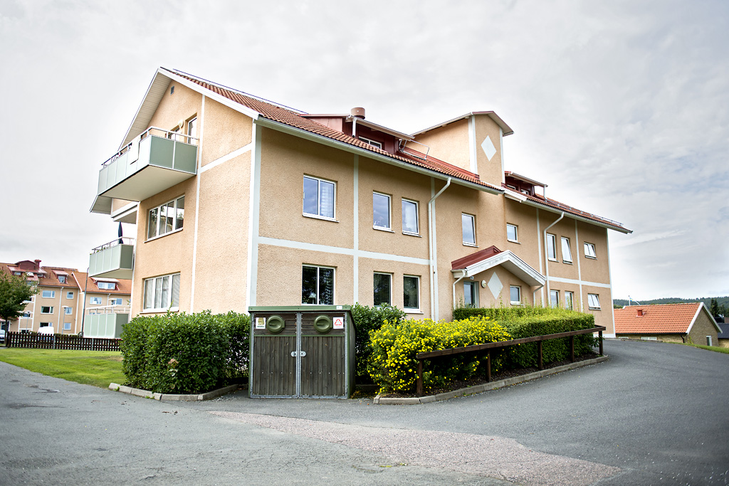 Gult putsat hyreshus med häckar framför